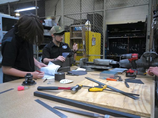 Three students recording final measurements and sketches in their engineering notebook.