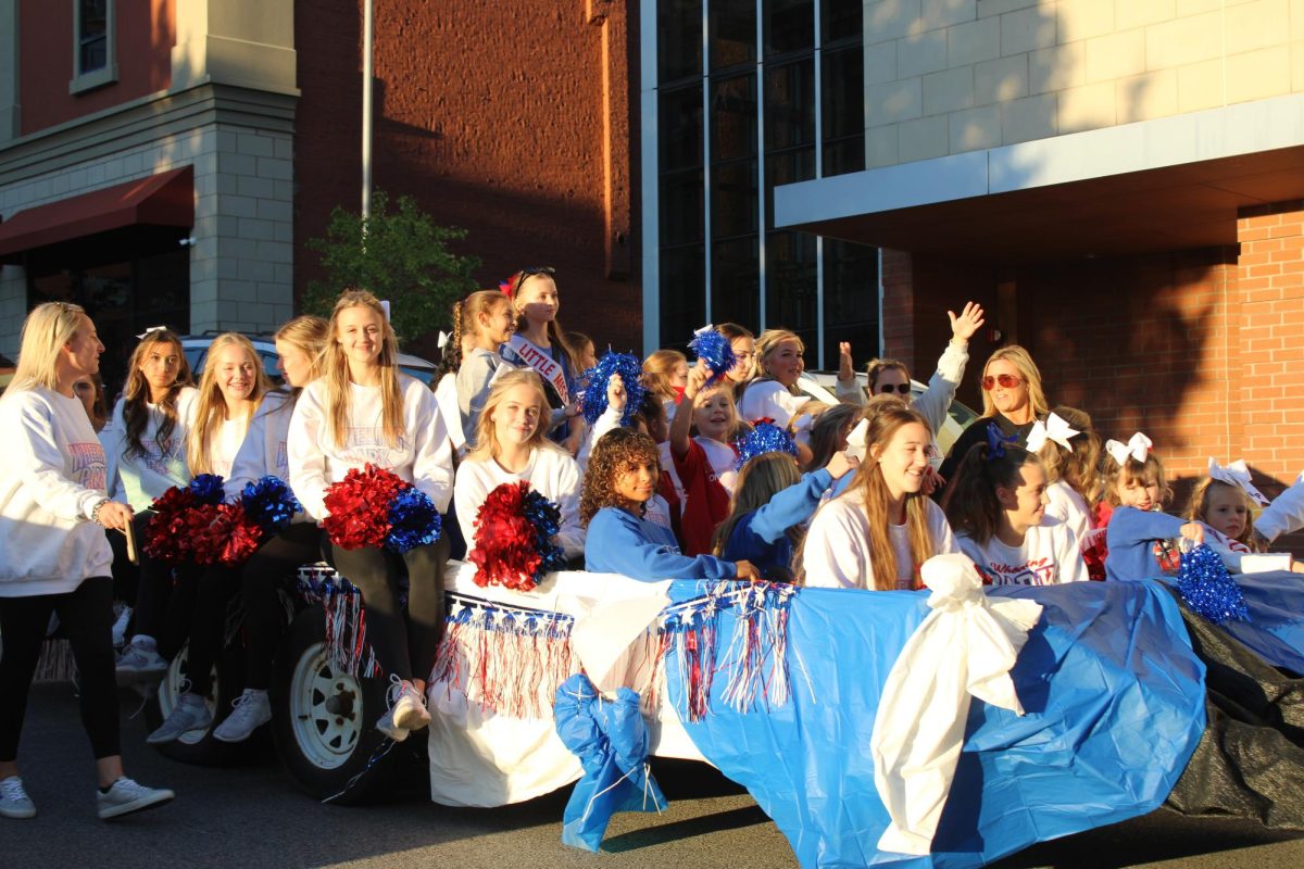 Cheerleaders and their "little miss" group ride through the streets.