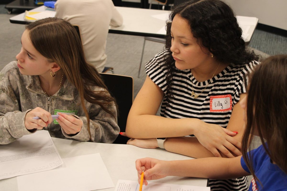 Lilly Smith works at a table in the KIVA as middle school students learn more about the over 15 events the speech and debate team competes in.