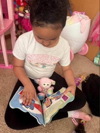 Cali tucked into a library book, her favorite stuffed animal nestled beside her.